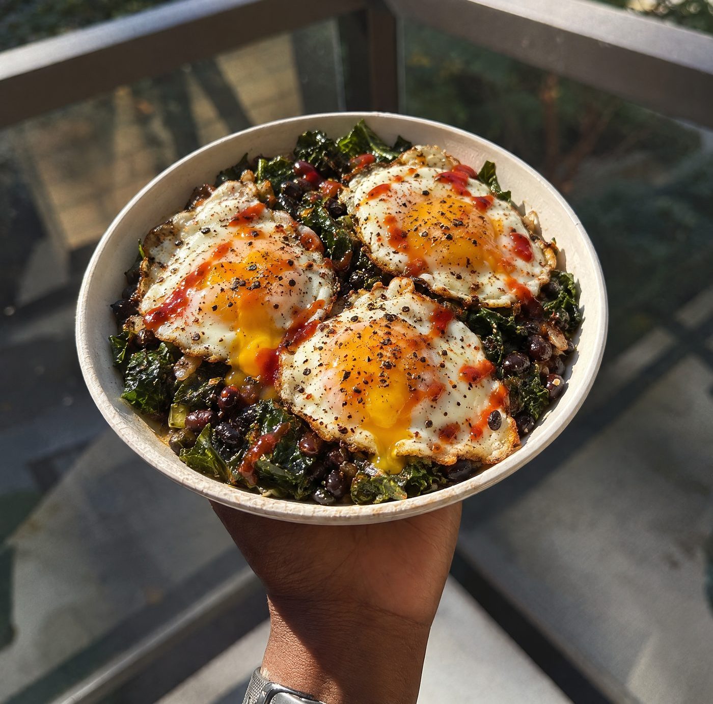 A bowl of greens and beans topped with three fried eggs and hot sauce