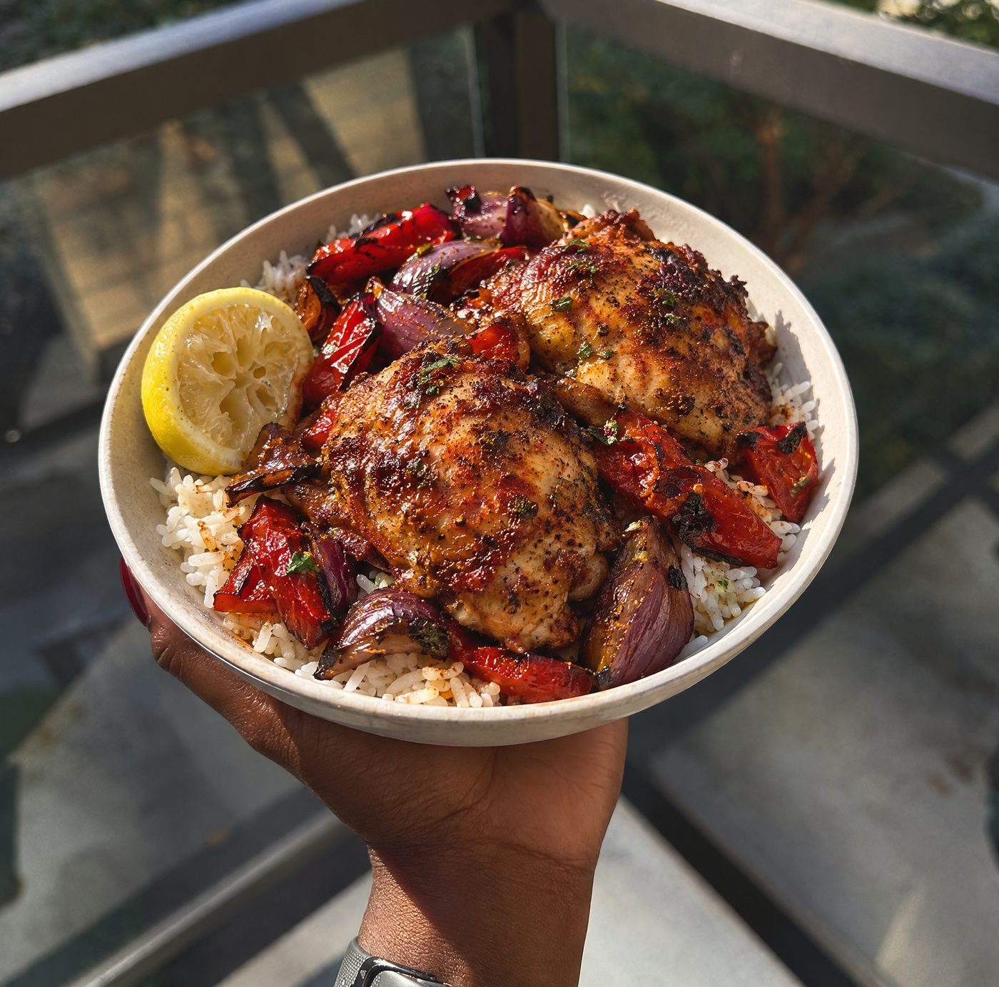 A bowl of paprika chicken thighs with roasted peppers and red onion over rice, with a wedge of lemon